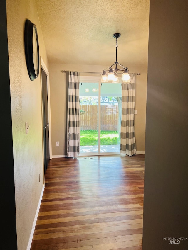unfurnished dining area with a textured ceiling, wood-type flooring, baseboards, a chandelier, and a textured wall