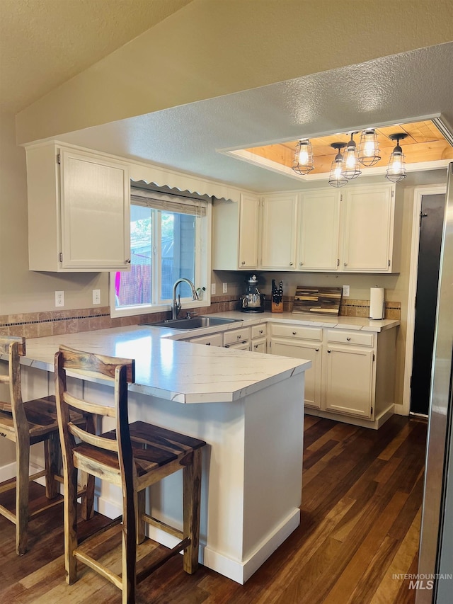 kitchen with a sink, a peninsula, white cabinetry, dark wood-type flooring, and a breakfast bar area