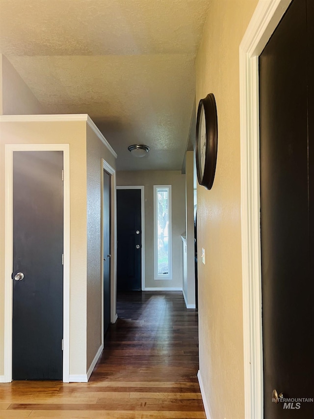 hallway featuring wood finished floors, a textured ceiling, and baseboards