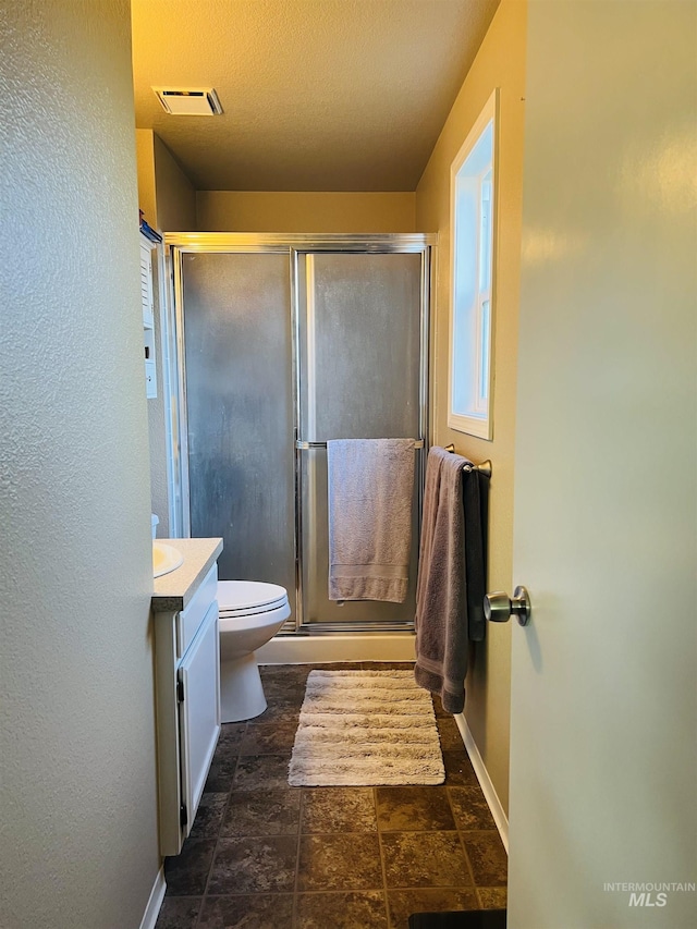 bathroom featuring baseboards, a stall shower, stone finish flooring, toilet, and vanity