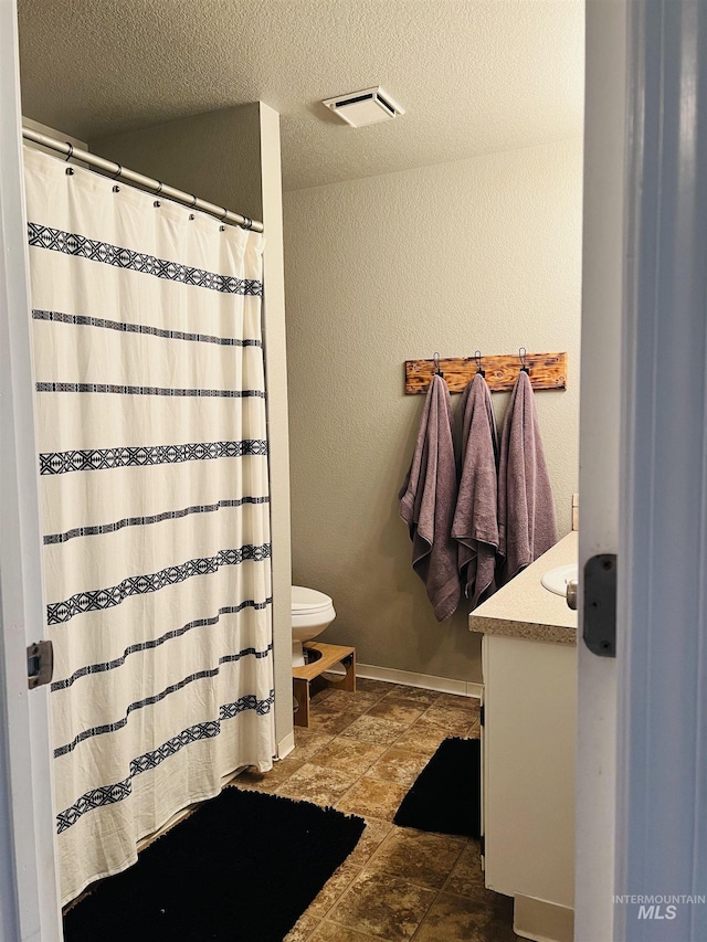 full bath featuring toilet, a textured wall, vanity, a textured ceiling, and baseboards