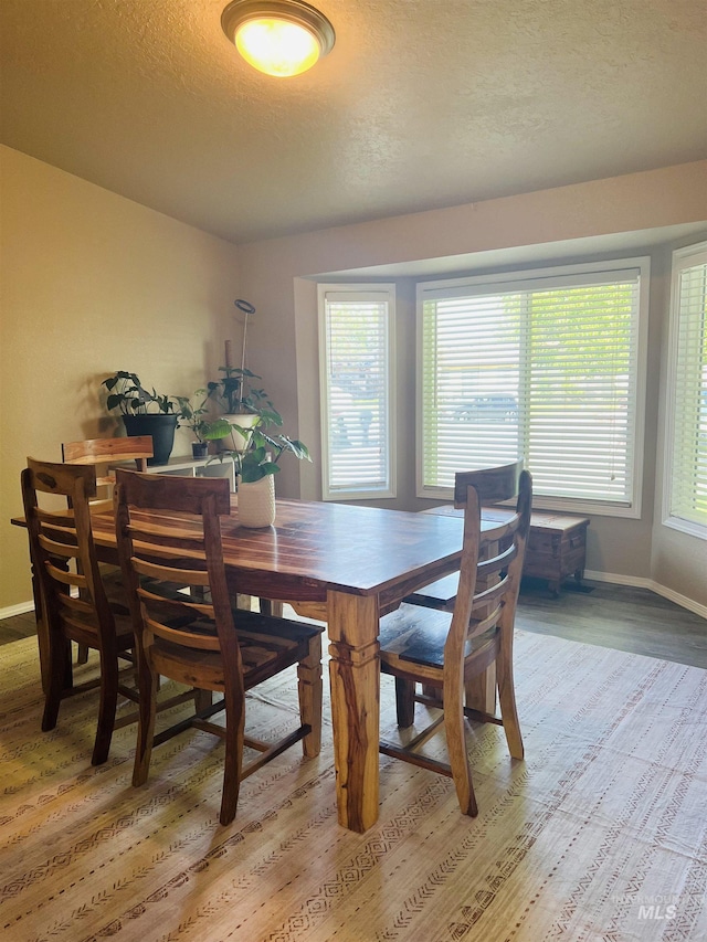 dining area featuring a textured ceiling, baseboards, light wood-type flooring, and healthy amount of natural light