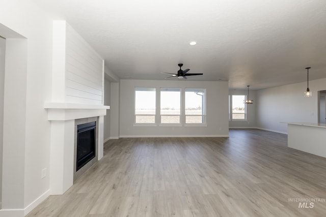 unfurnished living room featuring a ceiling fan, a large fireplace, light wood-style flooring, and baseboards