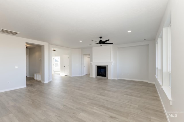 unfurnished living room featuring ceiling fan, light wood finished floors, a glass covered fireplace, and visible vents