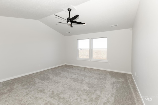 carpeted spare room featuring visible vents, vaulted ceiling, baseboards, and ceiling fan