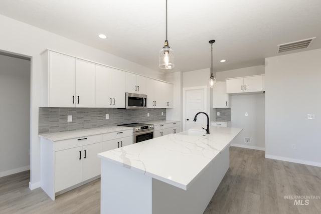 kitchen with light wood finished floors, stainless steel appliances, visible vents, white cabinets, and a sink