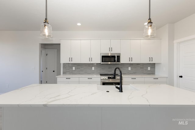 kitchen featuring stainless steel appliances, white cabinetry, decorative light fixtures, and tasteful backsplash