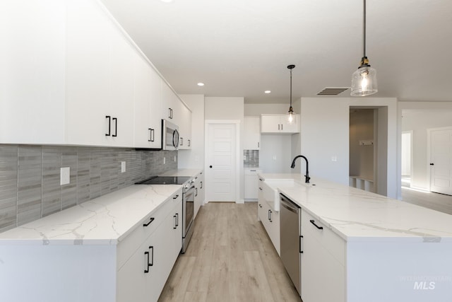 kitchen with light wood finished floors, white cabinets, decorative backsplash, appliances with stainless steel finishes, and hanging light fixtures