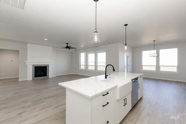 kitchen with visible vents, a glass covered fireplace, stainless steel dishwasher, light wood-style floors, and a sink