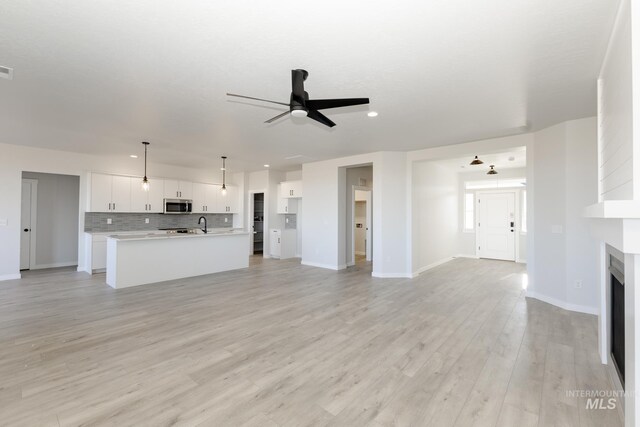 unfurnished living room with baseboards, a ceiling fan, light wood-type flooring, a fireplace, and recessed lighting