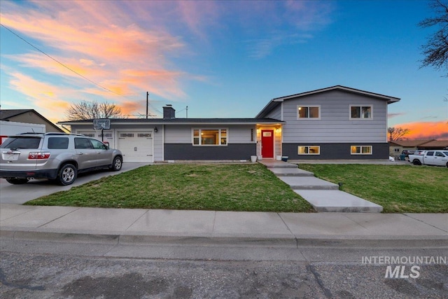 tri-level home with an attached garage, driveway, a chimney, and a front yard