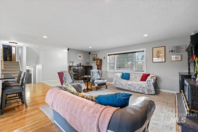 living area featuring baseboards, stairway, a textured ceiling, light wood-type flooring, and recessed lighting