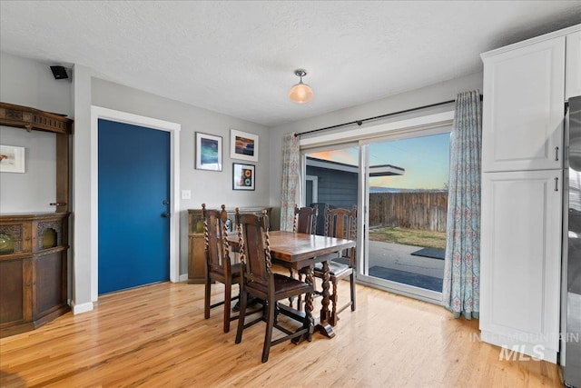 dining room with light wood-style floors, a textured ceiling, and baseboards