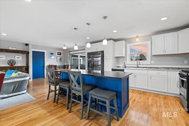 kitchen with stainless steel appliances, a sink, white cabinets, light wood-type flooring, and a kitchen bar