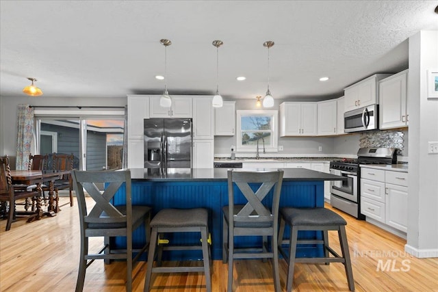 kitchen featuring appliances with stainless steel finishes, light wood-style floors, white cabinetry, a sink, and a kitchen bar