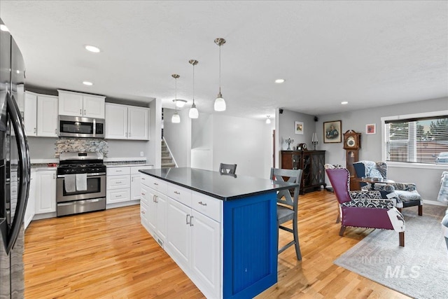 kitchen featuring a breakfast bar, light wood finished floors, stainless steel appliances, white cabinetry, and a kitchen island