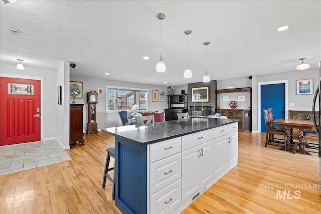 kitchen featuring dark countertops, light wood-style flooring, a kitchen island, a kitchen bar, and white cabinetry