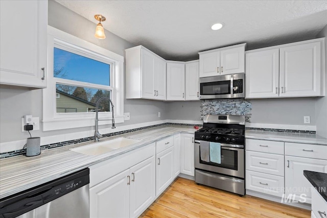 kitchen featuring light countertops, light wood-style flooring, appliances with stainless steel finishes, white cabinets, and a sink