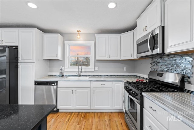 kitchen featuring white cabinets, light wood-type flooring, stainless steel appliances, and a sink