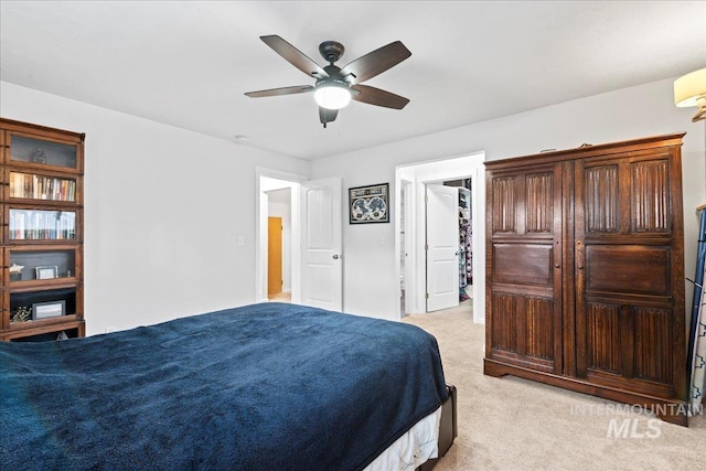 bedroom with a walk in closet, a ceiling fan, and light colored carpet