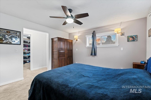 bedroom with baseboards, a walk in closet, a ceiling fan, and light colored carpet