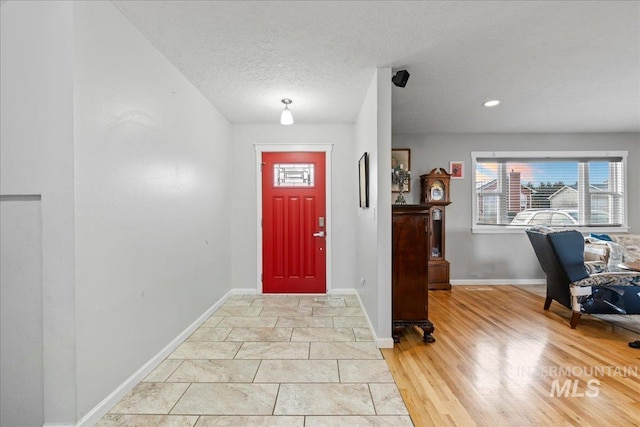 entrance foyer featuring light wood-style flooring, a textured ceiling, and baseboards