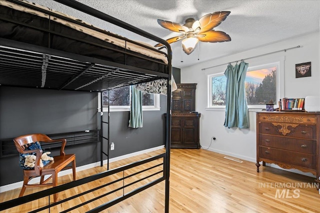 bedroom with a ceiling fan, a textured ceiling, baseboards, and wood finished floors