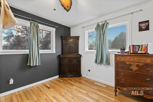 bedroom with a textured ceiling, wood finished floors, visible vents, and baseboards