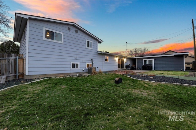 rear view of house with central air condition unit, fence, and a lawn