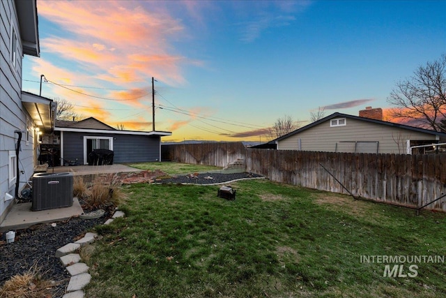 yard at dusk with a fenced backyard, central AC unit, an outdoor structure, and a patio