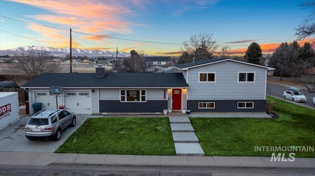 split level home featuring driveway, a chimney, an attached garage, a yard, and a mountain view