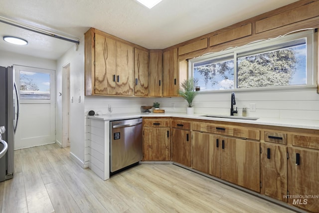 kitchen featuring stainless steel appliances, brown cabinetry, light countertops, and a sink