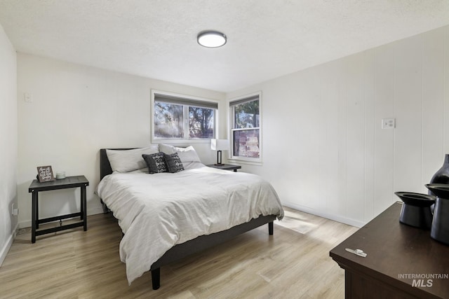 bedroom featuring baseboards, a textured ceiling, and light wood finished floors