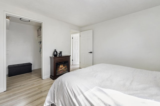 bedroom featuring a warm lit fireplace, light wood-type flooring, and baseboards