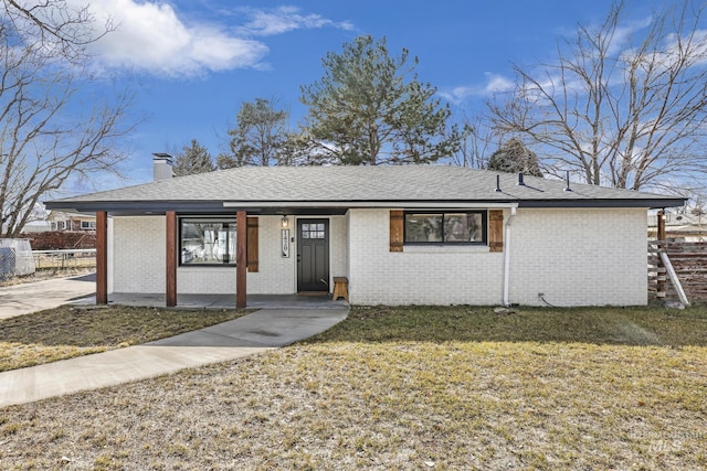 single story home featuring roof with shingles, brick siding, a chimney, and a front yard