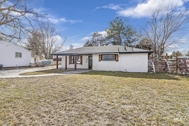 rear view of property featuring a yard, brick siding, a chimney, and fence