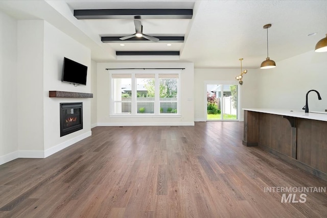 unfurnished living room featuring a glass covered fireplace, baseboards, wood finished floors, beam ceiling, and coffered ceiling