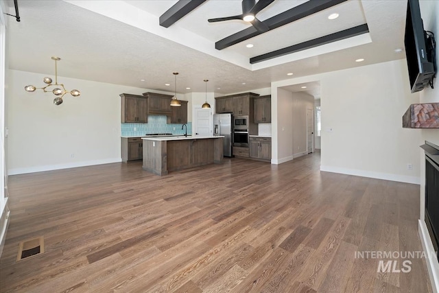 kitchen with appliances with stainless steel finishes, open floor plan, ceiling fan, light countertops, and backsplash