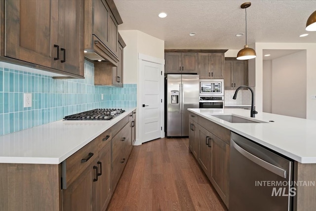 kitchen with appliances with stainless steel finishes, a sink, dark wood finished floors, light countertops, and decorative backsplash