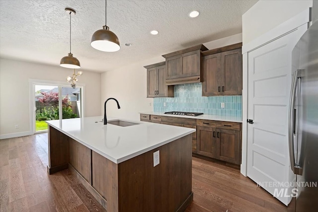 kitchen featuring a sink, dark wood-style flooring, decorative backsplash, a kitchen island with sink, and a textured ceiling