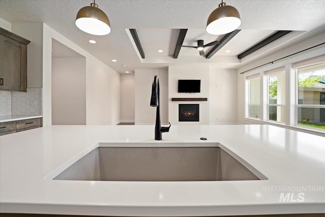 kitchen with a sink, open floor plan, light countertops, a warm lit fireplace, and tasteful backsplash