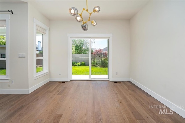 unfurnished dining area with wood finished floors, a chandelier, plenty of natural light, and baseboards