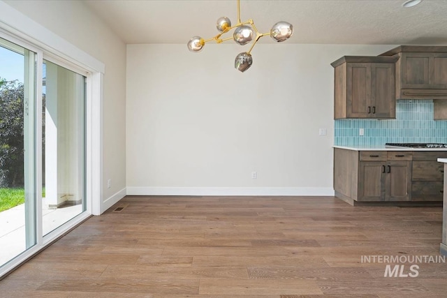 kitchen with a chandelier, light wood finished floors, decorative backsplash, light countertops, and baseboards