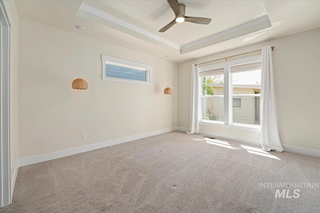 empty room with a tray ceiling, carpet flooring, ceiling fan, baseboards, and ornamental molding