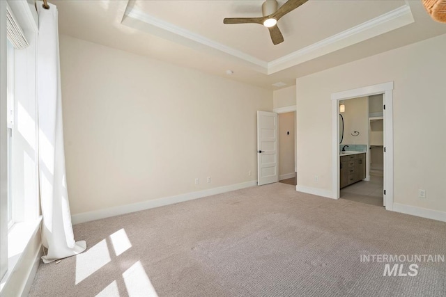 unfurnished bedroom featuring a tray ceiling, ornamental molding, light colored carpet, baseboards, and ensuite bathroom