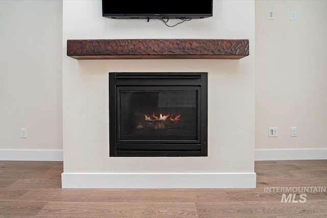 detailed view of wood finished floors, a lit fireplace, and baseboards