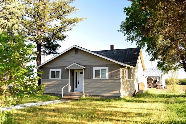 bungalow featuring a shingled roof, a chimney, and a front yard