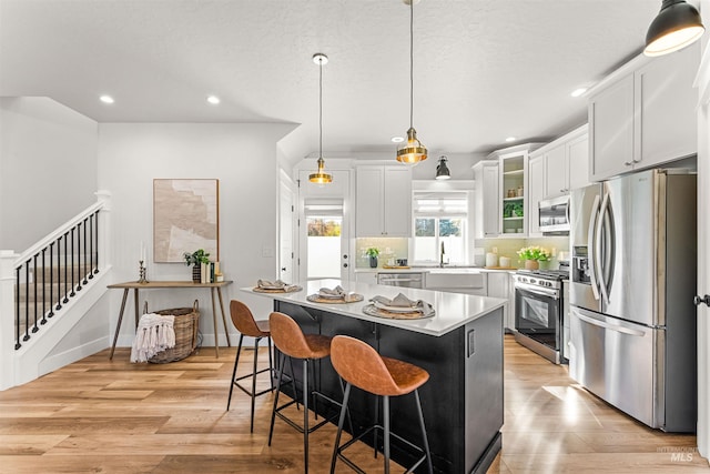 kitchen with glass insert cabinets, a center island, stainless steel appliances, light countertops, and white cabinetry