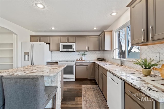 kitchen with white appliances, light stone countertops, dark hardwood / wood-style floors, sink, and backsplash