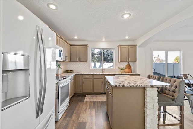 kitchen featuring white appliances, light stone countertops, a center island, tasteful backsplash, and a kitchen breakfast bar